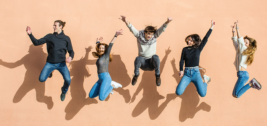 A group of friends jumping with their hands in the air laughing and smiling